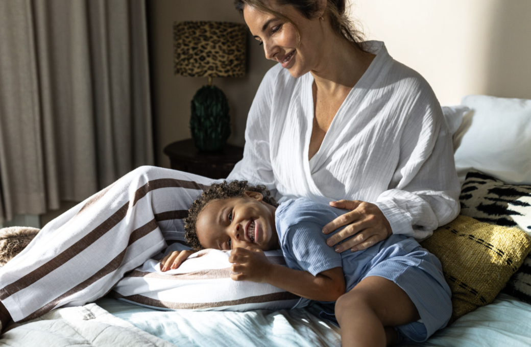 Een moeder ligt lachend met haar kind op bed
