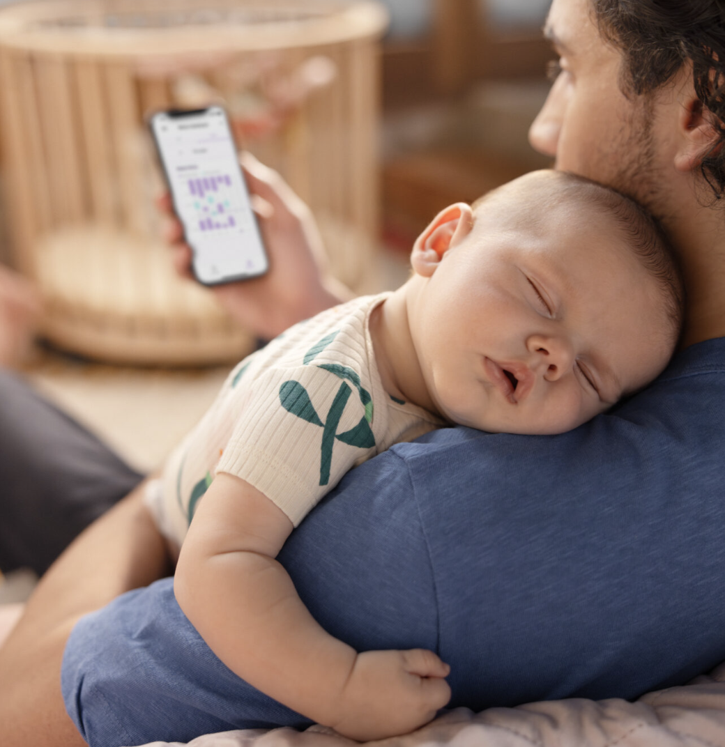 Een vader met een slapende baby op zijn schouder kijkt op zijn telefoon