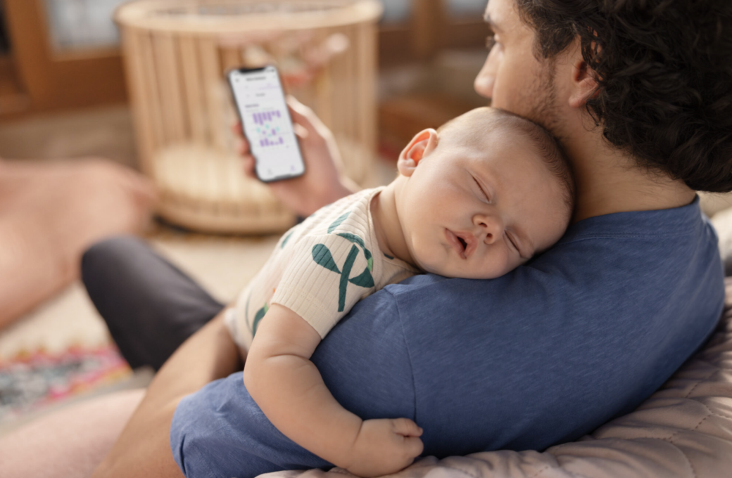 Een vader met een slapende baby op zijn schouder kijkt op zijn telefoon