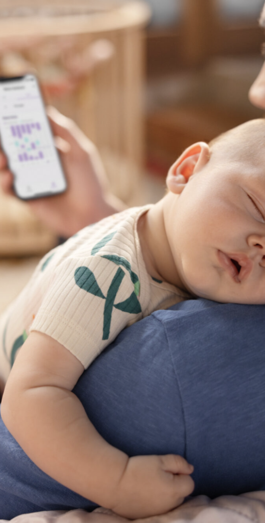 Een vader met een slapende baby op zijn schouder kijkt op zijn telefoon