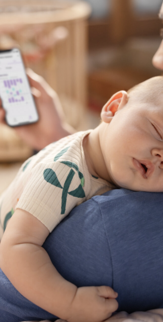 Een vader met een slapende baby op zijn schouder kijkt op zijn telefoon