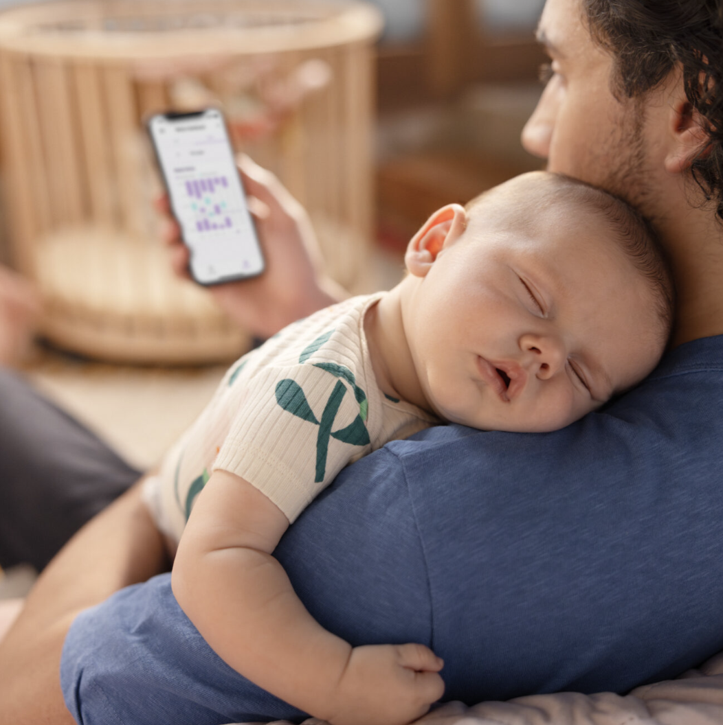 Een vader met een slapende baby op zijn schouder kijkt op zijn telefoon